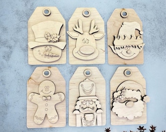 May include: Six unfinished wooden Christmas gift tags with various holiday characters. The tags feature a snowman, reindeer, elf, gingerbread person, nutcracker, and Santa Claus.