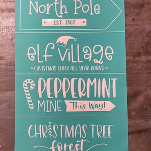 May include: A teal blue sign with white text that reads "North Pole EST. 1863", "elf Village - CHRISTMAS CHEER ALL YEAR ROUND", "PEPPERMINT MINE This Way!" and "CHRISTMAS TREE forest".