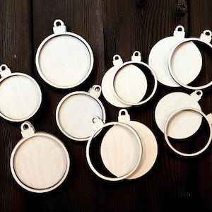 May include: A collection of unfinished wooden Christmas ornament blanks. The ornaments are round with a circular frame and a small loop at the top for hanging. Some have a full circle, while others have a partial circle cut out.