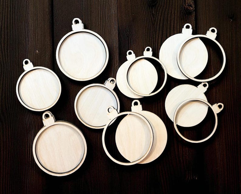 May include: A collection of unfinished wooden Christmas ornament blanks. The ornaments are round with a circular frame and a small loop at the top for hanging. Some have a full circle, while others have a partial circle cut out.