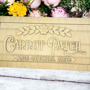 May include: A wooden sign with the words "Carrot Patch" and "Peter Cottontail Farms" in a decorative font. The sign is decorated with a carved flower and leaves.