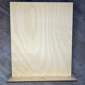 May include: A blank, light brown wooden sign with a natural wood grain pattern. The sign is standing on a small, light brown wooden base.