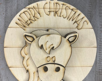 Puede incluir: Un adorno navideño de madera con un diseño de cabeza de caballo y el texto "Merry Christmas" alrededor del borde.
