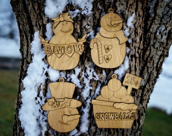 May include: Four wooden ornaments shaped like snowmen and a bucket of snowballs. The snowmen have different facial features and accessories. One snowman has a banner that says "SNOW". Another snowman has a candy cane and two hearts. The bucket of snowballs has a sign that says "25c SNOWBALLS".