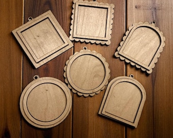 May include: A collection of five unfinished wooden frames in various shapes: square, round, and arched. Each frame has a small hole at the top for hanging. The frames are arranged on a wooden surface.