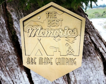 May include: A wooden sign with the text "The Best Memories Are Made Camping" in a rustic font. The sign features a stylized image of a tent, a campfire, and trees.