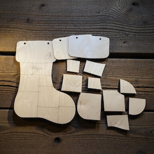 May include: A disassembled wooden Christmas stocking puzzle with various geometric shapes. The stocking is made of multiple rectangular pieces. Additional wooden pieces are scattered around the stocking, ready to be assembled. The wood has a natural, light color.