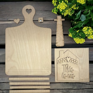 May include: Wooden cutting board with a heart cutout, a small heart-shaped tag, and a sign that reads "This is us" with a heart and leaves around the text.