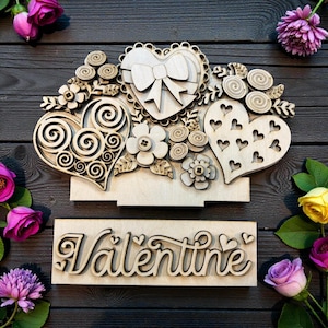 May include: Wooden Valentine's Day decoration featuring laser-cut hearts, flowers, and a bow. The word "Valentine" is also cut from wood. The design is set against a dark wood background, with pink and yellow roses surrounding the decoration.