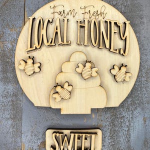May include: Wooden sign with the text "Farm Fresh Local Honey" and a honeycomb design with bees. A separate wooden sign below reads "Sweet".