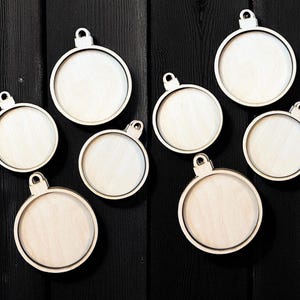 May include: A collection of eight unfinished wooden Christmas ornament blanks. Each ornament is round with a small loop at the top for hanging. The ornaments are made of light-colored wood and are arranged on a dark wooden surface.