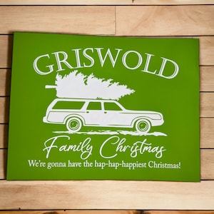 May include: Green sign with white text that reads "Griswold Family Christmas" with a white illustration of a station wagon with a Christmas tree on top. The text below the illustration reads "We're gonna have the hap-hap-happiest Christmas!"