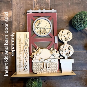 May include: Wooden farmhouse-style decor featuring a red door with a "Hello" sign, a basket with a lemon, and a topiary. The words "fresh squeezed lemons" are displayed on a separate sign. The decor is set on a wooden shelf.