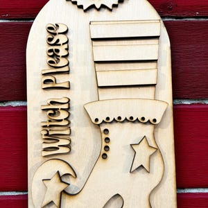 May include: Wooden Halloween sign featuring a witch's boot, a bat, and the words "Witch Please." The sign is made of light-colored wood and has a rustic, carved design. The boot has a star and decorative details.