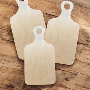 May include: Three wooden cutting boards with handles. The boards are light brown and have a smooth surface.