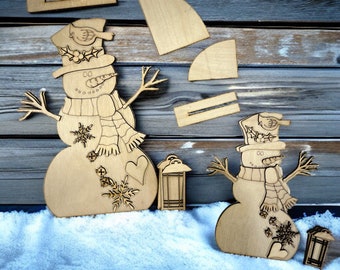 May include: Wooden snowman cutouts with intricate details, including a hat, scarf, and snowflake accents. The image also shows small wooden lanterns and additional wooden pieces, all set against a snowy backdrop and a rustic wooden wall.