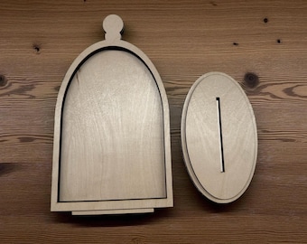 May include: Two wooden pieces, one arched and one oval, with a slot. The arched piece has a rounded top and a black outline. The oval piece has a vertical slot. Both pieces are made of light-colored wood.