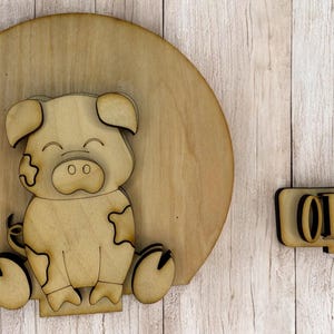 May include: Wooden cutout of a pig with a smiling face and the word "OINK" on a separate wooden cutout.