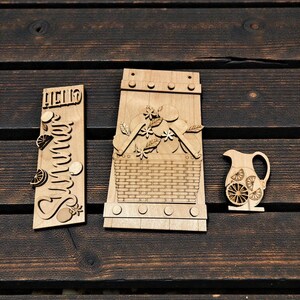 May include: Wooden laser-cut summer-themed decor. Includes a sign with "Hello Summer" text, a picnic basket, and a pitcher with lemon slices. The items are made of light-colored wood and are arranged on a dark wooden surface.