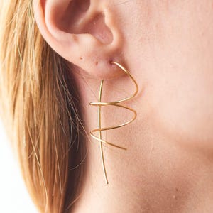 Könnte beinhalten: Goldfarbene, abstrakte Ohrringe aus Draht mit einem Spiraldesign. Die Ohrringe sind lang und hängen vom Ohrläppchen.