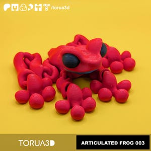 May include: A bright red articulated frog figurine with large, smooth black eyes. The surface shows visible 3D printed layer lines. The frog has a segmented body and limbs designed for movement. Text at the top reads /torua3d and at the bottom TORUA3D ARTICULATED FROG 003.