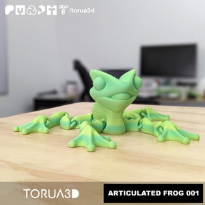 May include: A green and yellow articulated frog figurine. The frog has a wide mouth and large eyes. The figurine is made of plastic and is about 12.5 cm long.