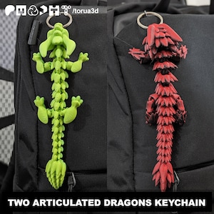 Może przedstawiać: Dwa breloczki z ruchomymi smokami. Jeden jest limonkowo-zielony, drugi czerwony. Oba są przymocowane do srebrnych kółek na klucze. Smoki są drukowane w 3D i mają segmentową konstrukcję. Tekst na dole brzmi "TWO ARTICULATED DRAGONS KEYCHAIN".