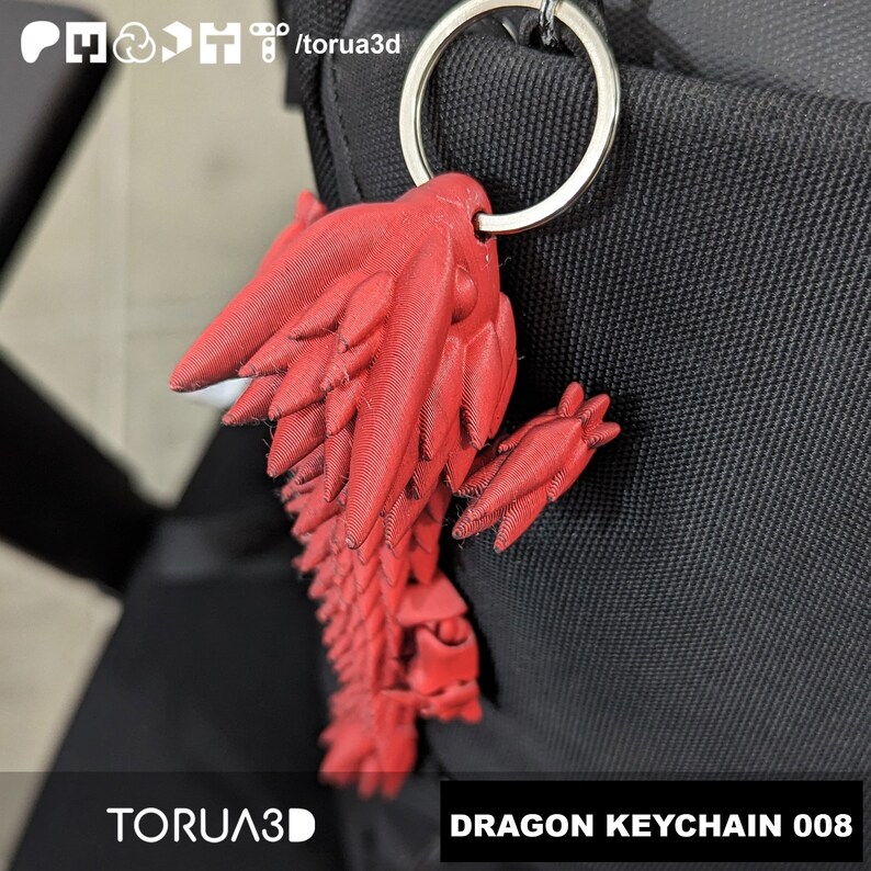 May include: A red dragon keychain with a silver keyring attached. The dragon is 3D-printed and has detailed wings and a tail. The text "DRAGON KEYCHAIN 008" is visible on the bottom right. The brand name "TORUA3D" is also visible.