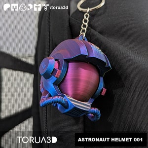 May include: A blue and purple astronaut helmet keychain with a silver chain. The helmet has a red visor and a textured surface. The keychain is labeled "ASTRONAUT HELMET 001".