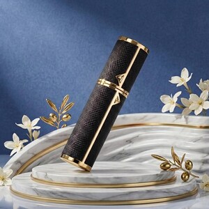 May include: A black and gold perfume atomizer with a textured pattern. The cylindrical container has gold accents and a decorative design. It is displayed on a marble and gold platform with floral accents, set against a blue backdrop.