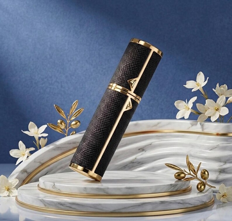 May include: A black and gold perfume atomizer with a textured pattern. The cylindrical container has gold accents and a decorative design. It is displayed on a marble and gold platform with floral accents, set against a blue backdrop.
