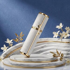 May include: A white and gold perfume atomizer with a textured surface. The cylindrical container has gold accents and a decorative design. The atomizer is displayed on a marble platform with floral accents, creating an elegant presentation.
