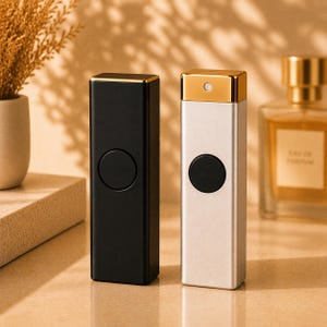 Peut inclure: Deux vaporisateurs de parfum rectangulaires posés verticalement. L'un est noir mat avec un sommet doré et un bouton noir circulaire. L'autre est argenté avec un sommet doré et un bouton noir circulaire. Tous deux ont un design vertical épuré.