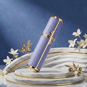 May include: A lavender-colored perfume atomizer with gold accents. The cylindrical case has a textured leather-like appearance and is trimmed with gold. The atomizer is displayed on a marble and gold tiered platform, with white flowers and gold olive branch decorations.