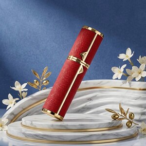 May include: A red, textured, cylindrical container with gold accents. The container has a gold band in the middle and at both ends. The design includes gold vertical lines and a gold triangle at the top and bottom of the container.