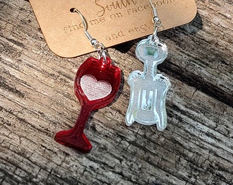 May include: A pair of earrings featuring a red wine glass and a silver corkscrew. The earrings are hanging from a brown card with the text "15 South find me on facebook and etsy".