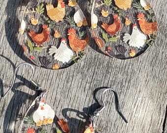 May include: A pair of teardrop-shaped earrings with a chicken and egg pattern. The earrings are made of clear resin and have silver hooks.