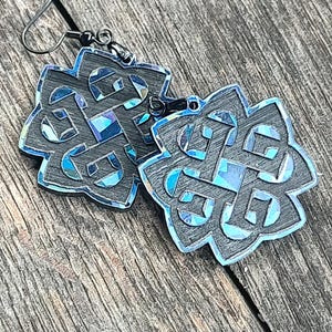 May include: A pair of black earrings with a blue iridescent finish. The earrings are shaped like a Celtic knot.