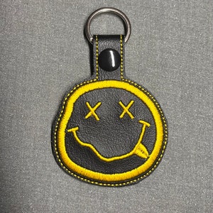May include: Black leather keychain with a yellow stitched smiley face with X's for eyes.