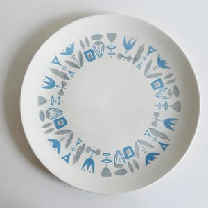 May include: White ceramic plate with a decorative border of stylized blue and gray floral and geometric shapes. The plate has a clean, modern design, suitable for serving food.