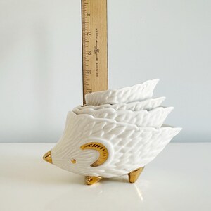 May include: A white ceramic hedgehog-shaped measuring cup set with gold accents. The set includes four nesting cups, each shaped like a leaf. The hedgehog has gold feet, a gold eye, and a gold crescent moon design.