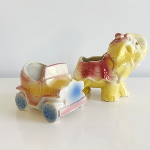 May include: Two vintage ceramic planter figurines, one shaped like a car and the other like an elephant. The car is yellow, pink, and blue, while the elephant is yellow, pink, and red.