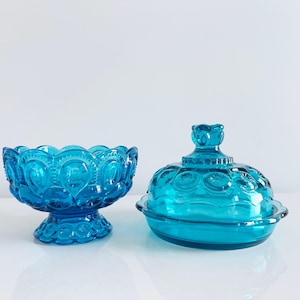 May include: Two pieces of turquoise glass tableware. One is a footed bowl with a scalloped rim. The other is a covered dish with a decorative knob on top. Both pieces have a textured, embossed pattern.