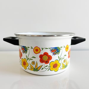 May include: White enamel pot with black handles and a floral design featuring red, yellow, blue, and green flowers.