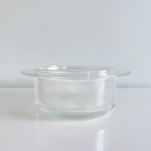 May include: A clear glass bowl with a wide, flat rim and a textured, ribbed interior. The bowl is empty and sits on a white surface.