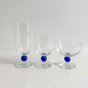 May include: Three clear glass drinking glasses with blue glass bases. The glasses are different sizes and shapes.