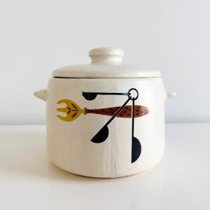 May include: White ceramic crock pot with a lid and a black and brown abstract design of a fork and spoon.