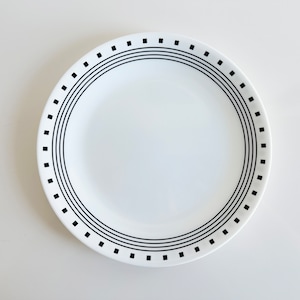 May include: A white ceramic dinner plate with a black geometric design around the rim.