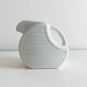 May include: White ceramic pitcher with a rounded body and a handle. The pitcher has a textured, ribbed design.