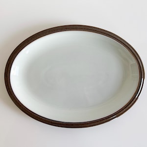 May include: A white oval serving platter with a brown rim. The platter is made of ceramic and has a smooth, glossy finish.